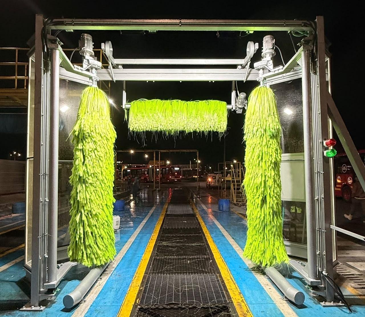 Túnel de lavado industrial Metgal en operación durante la noche, con cepillos verdes y buses del Sistema Integrado de Transporte al fondo
